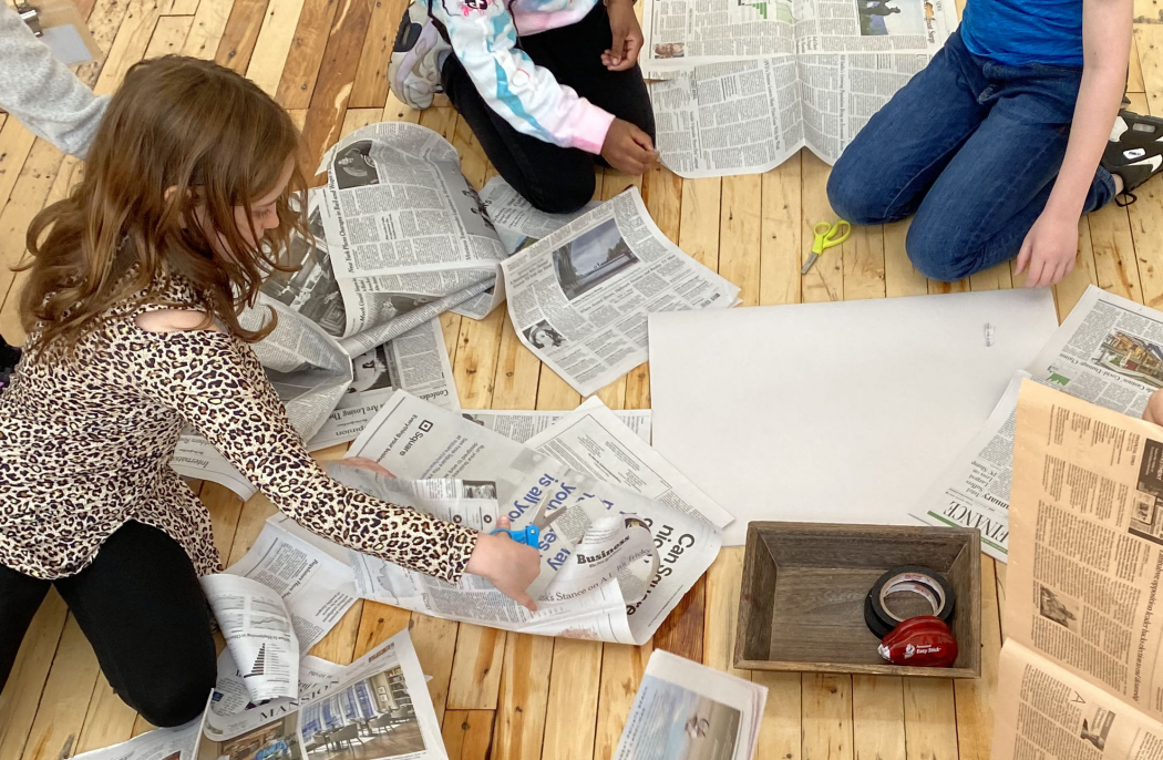 Children cut up newspapers on hardwood floor